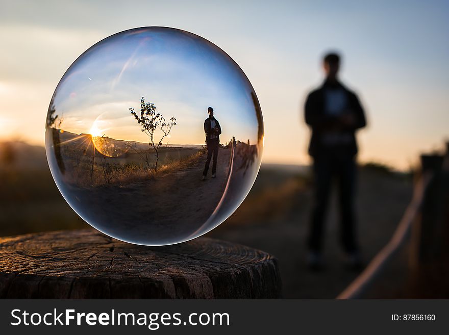 Silhouetted person in countryside at sunset viewed from back with front view of person reflected in glass ball. Silhouetted person in countryside at sunset viewed from back with front view of person reflected in glass ball.