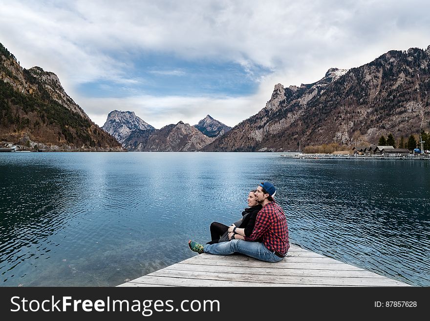 Couple sitting on a wooden pier on a lake and mountains in the background. Couple sitting on a wooden pier on a lake and mountains in the background.