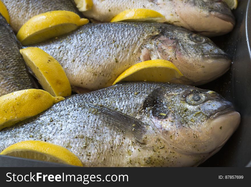 Sea bream fishes ready to be baked in oven with lemon wedges.