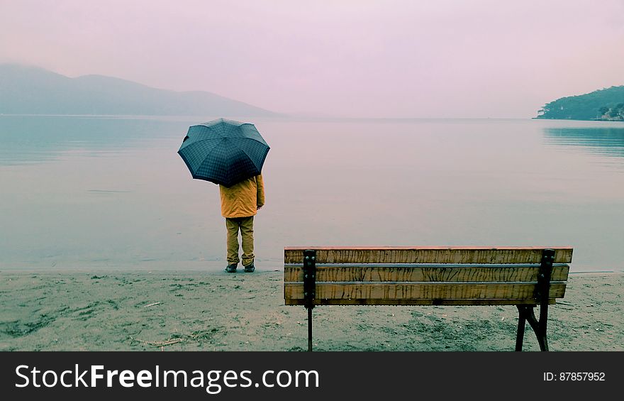 Wet misty day with poor visibility and man beside the sea in yellow jacket holding dark colored umbrella. Wet misty day with poor visibility and man beside the sea in yellow jacket holding dark colored umbrella.