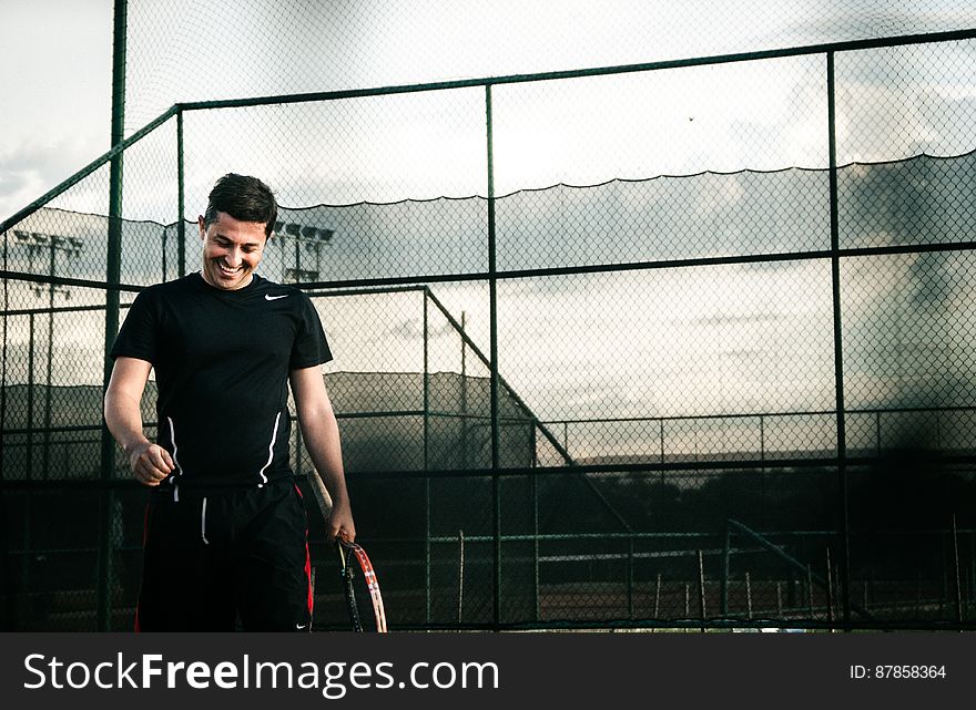 A smiling man out on the tennis court with a tennis racket in hand. A smiling man out on the tennis court with a tennis racket in hand.