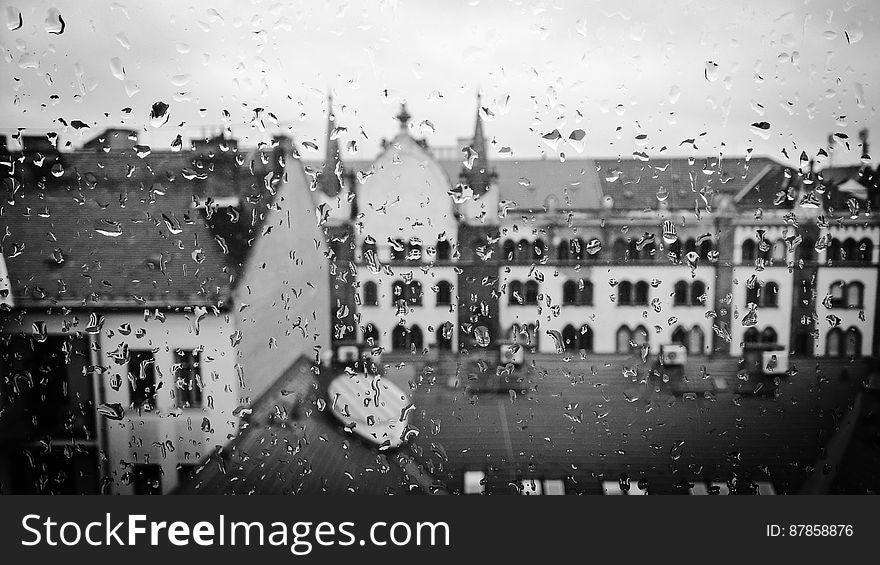 Historic buildings in Hungary seen through a window covered in rain drops, gray sky.