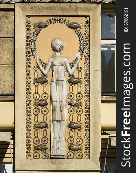 A building decoration in Art Nouveau style, representing a longiline woman figure surrounded by fishes connected by chain links. A building decoration in Art Nouveau style, representing a longiline woman figure surrounded by fishes connected by chain links.