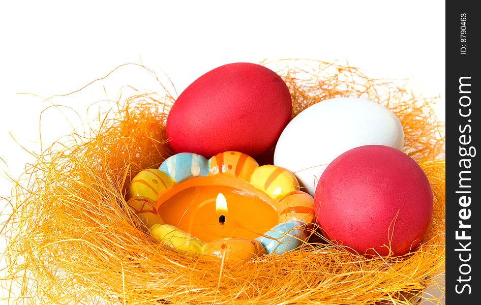 Eggs and candle in a small nest on white background