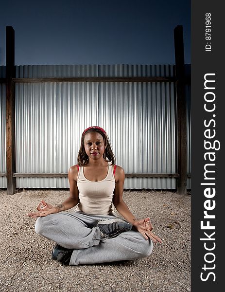 African-American woman meditating in front of corrugated metal