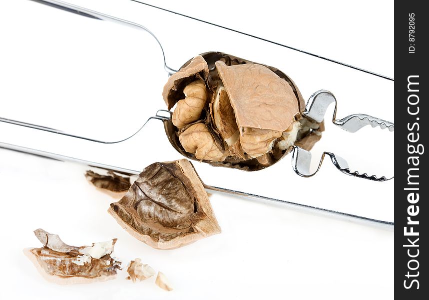 Metal nutcracker with crushed walnuts on white background