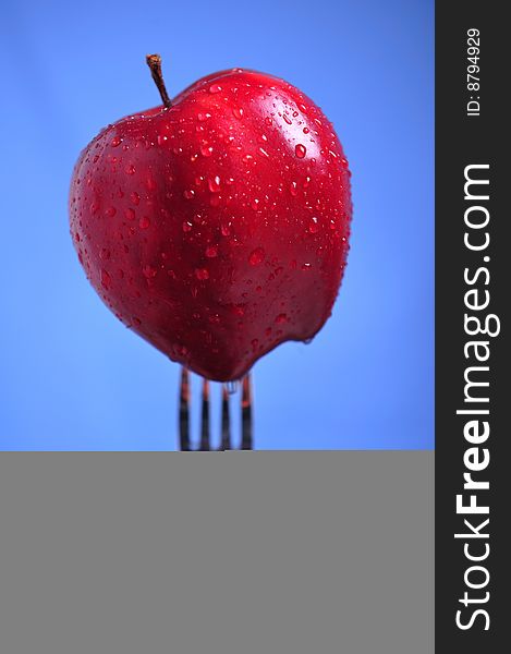 Red apple covered with drops of water on fork, blue background