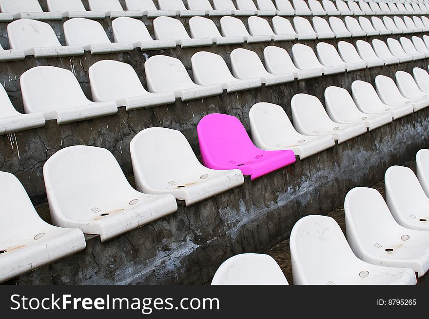 Plastic armchairs on a stadium tribune. One place pink in white section. Plastic armchairs on a stadium tribune. One place pink in white section.