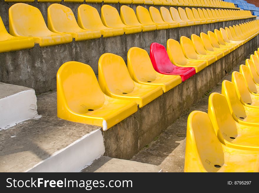 Plastic armchairs on a stadium tribune. One place in section is allocated with other colour. Plastic armchairs on a stadium tribune. One place in section is allocated with other colour.