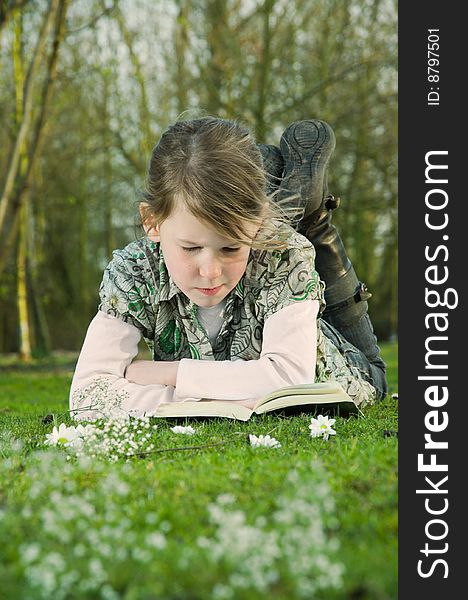Image of a young girl with a book on the grass in spring. Image of a young girl with a book on the grass in spring.