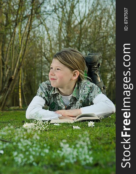 Image of a young girl with a book on the grass in spring. Girl looking dreamy. Image of a young girl with a book on the grass in spring. Girl looking dreamy.
