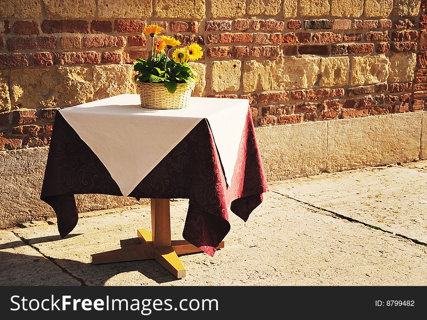 Lonely table with flowers against old brick wall in warm sunlight. The picture was made in Verona, Italy