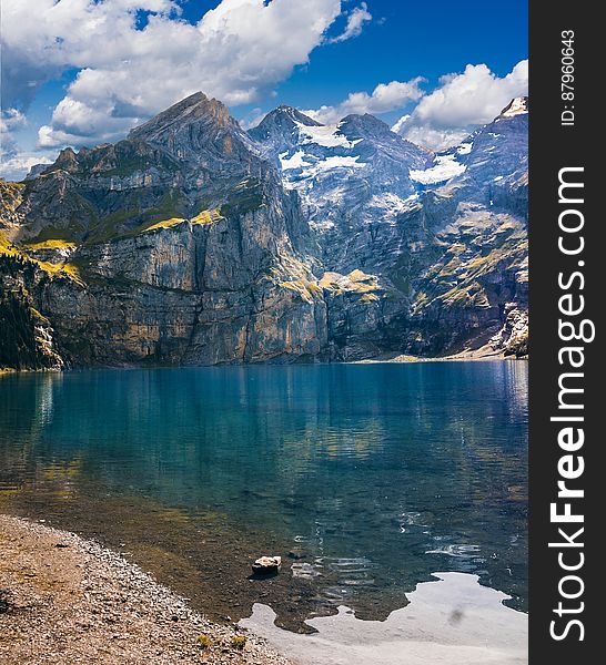 Banks of clear alpine lake surrounded by mountain peaks against blue skies on sunny day. Banks of clear alpine lake surrounded by mountain peaks against blue skies on sunny day.