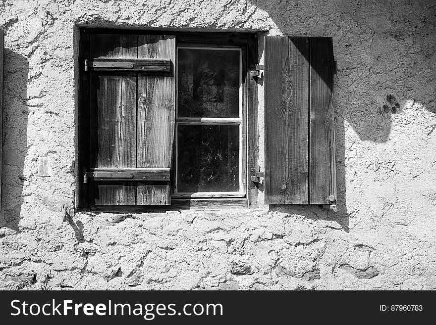 Close up of rustic wooden shutters on window in concrete wall in black and white.
