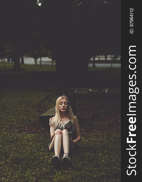 Woman with closed eyes sitting in grass at park in evening. Woman with closed eyes sitting in grass at park in evening.