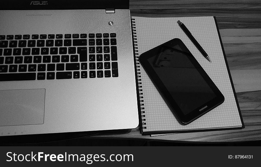 Black and white closeup of laptop, smartphone and notebook with pen on table. Black and white closeup of laptop, smartphone and notebook with pen on table.