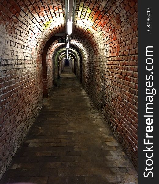 Brick underground passage in old building receding into distance.