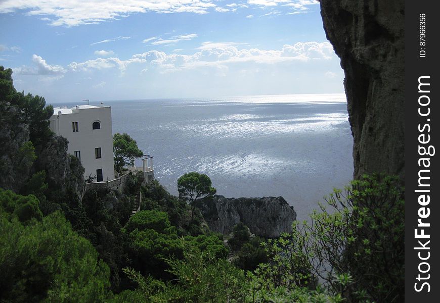 Coastal view from a steep wooded cliff of the tranquil sea with a modern building (apartments) built into the hillside. Coastal view from a steep wooded cliff of the tranquil sea with a modern building (apartments) built into the hillside.