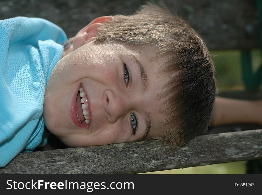 Young boy smiling while lying on a park bench. Young boy smiling while lying on a park bench.