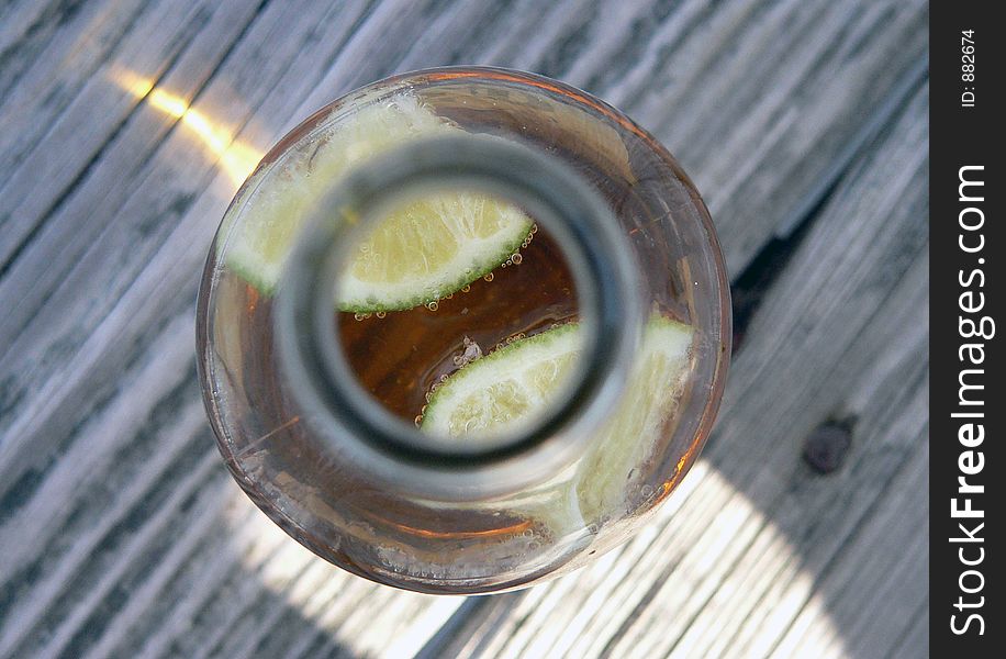 A top-down shot of a beer bottle focusing on delicious limes surrounded by carbonated bubbles on a wooden deck at the beach / ocean. A top-down shot of a beer bottle focusing on delicious limes surrounded by carbonated bubbles on a wooden deck at the beach / ocean.