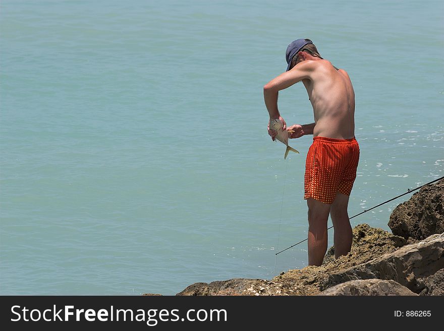 Man fishing on beach catches fish by hooking him on side. Man fishing on beach catches fish by hooking him on side