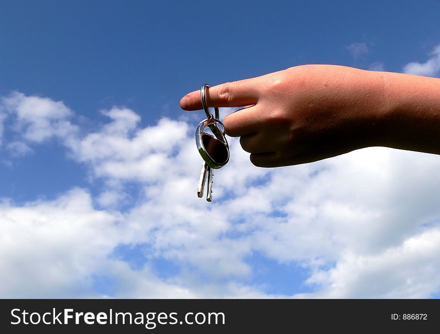Holding key against a blue sky with clouds