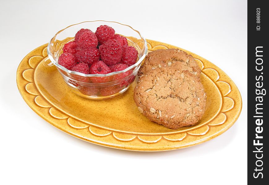 A snack of raspberries and cookies rests on a yellow dish. A snack of raspberries and cookies rests on a yellow dish.