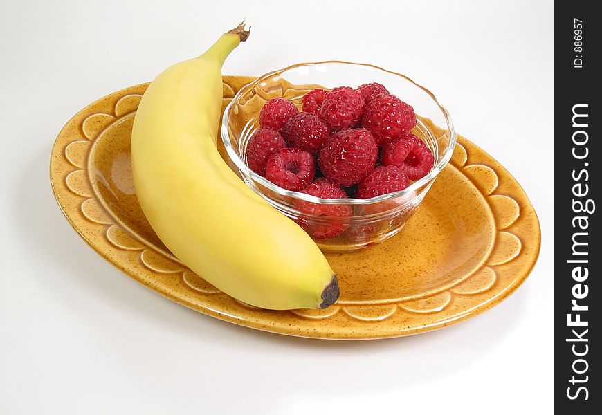 A snack of  banana and raspberries rests on a yellow plate. A snack of  banana and raspberries rests on a yellow plate.