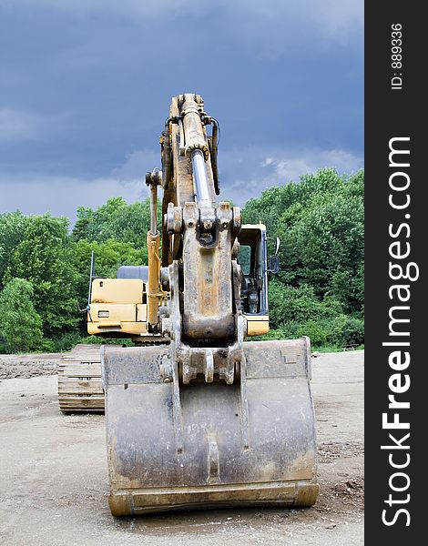 A Backhoe parked at the construction scene - storm brewing - cloudy dramatic sky. A Backhoe parked at the construction scene - storm brewing - cloudy dramatic sky.