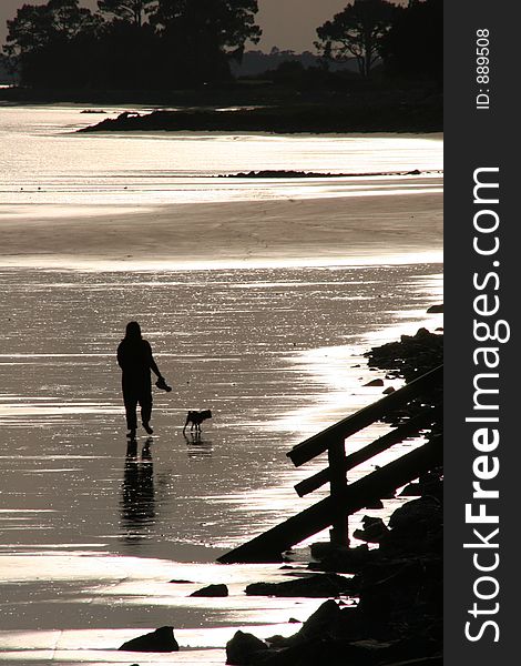 Silhouette of woman walking dog on beach at sunset. Silhouette of woman walking dog on beach at sunset