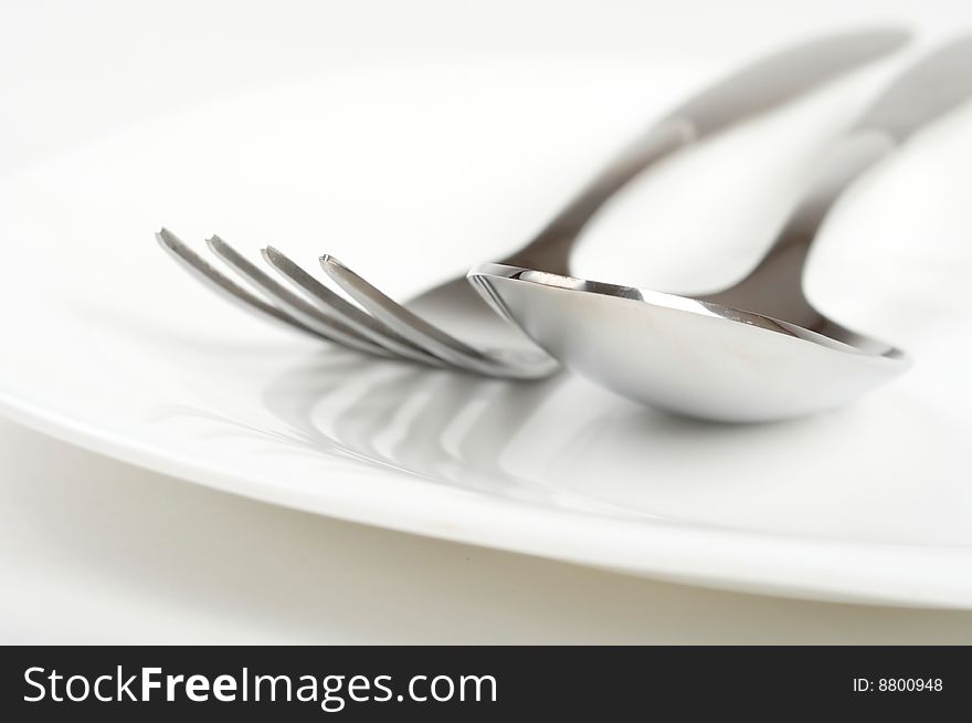 Photo of fork and spoon on white plate. Photo of fork and spoon on white plate