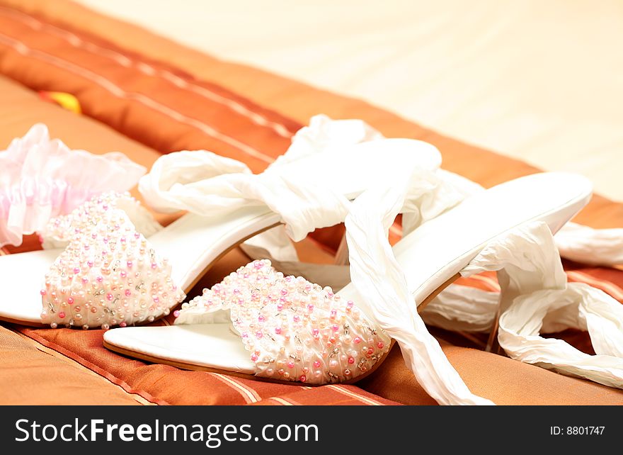 White bridal shoes adorned with pink, white and silver beads lying on brown bed cover. White bridal shoes adorned with pink, white and silver beads lying on brown bed cover