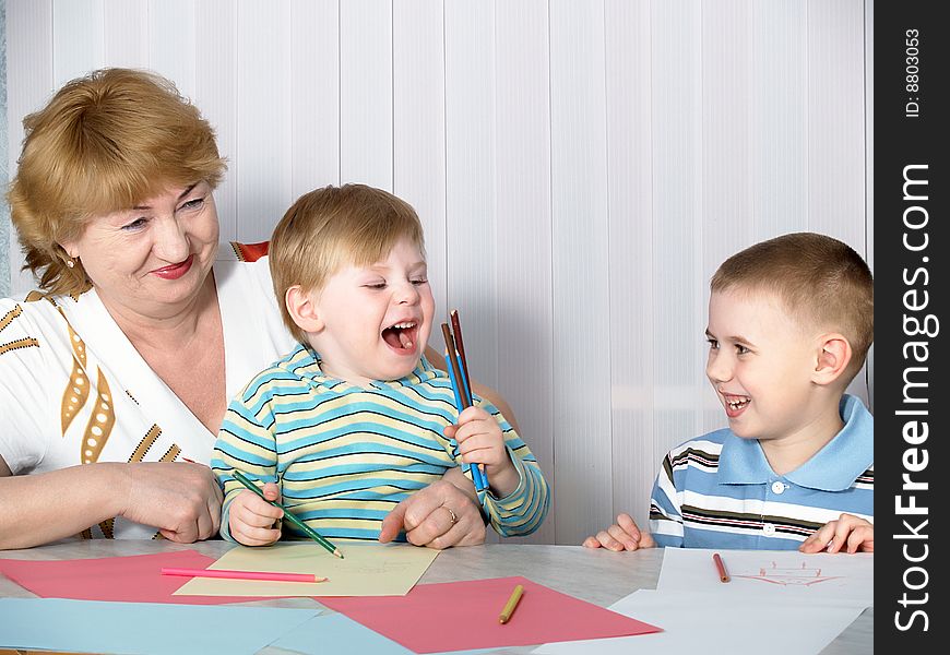 The grandmother is engaged in drawing with two grandsons. The grandmother is engaged in drawing with two grandsons