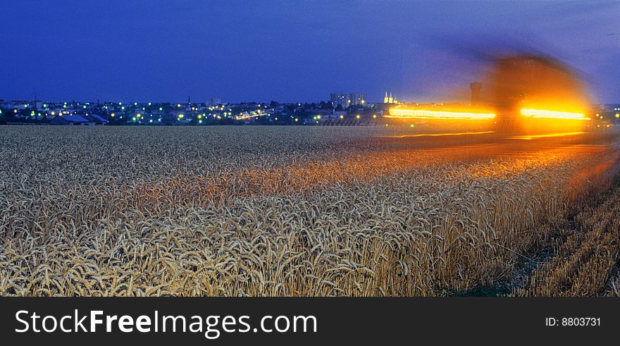Harvester at work in the dark, near a city