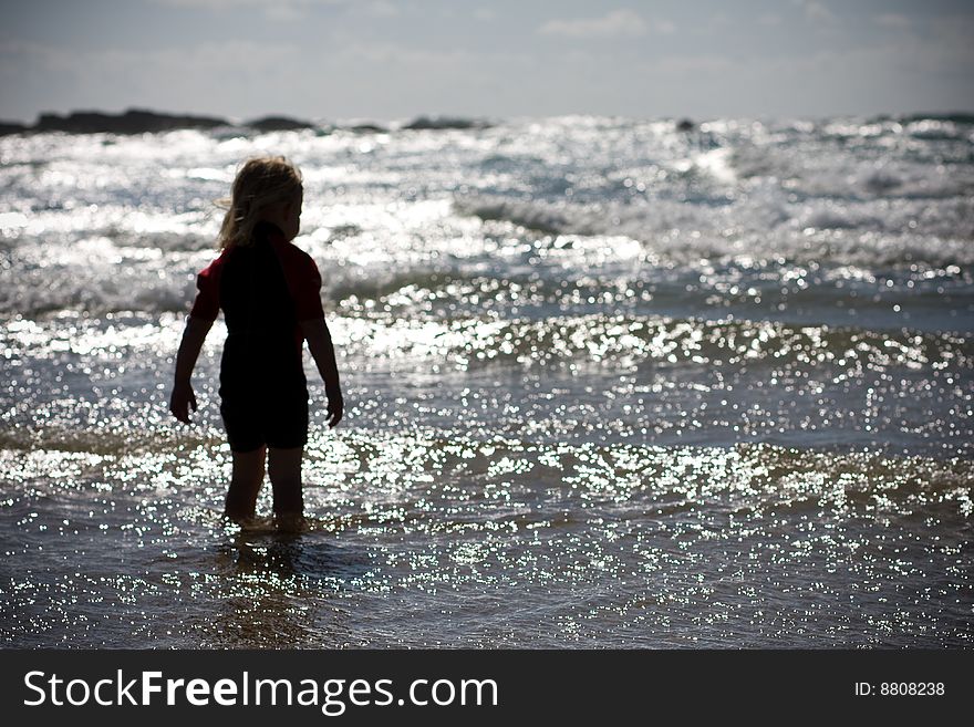 Silouette of child standing in the surf staring out to sea. Silouette of child standing in the surf staring out to sea