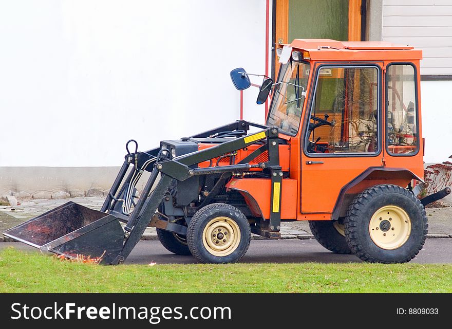 Orange tractor with scoop bucket in the suburbs