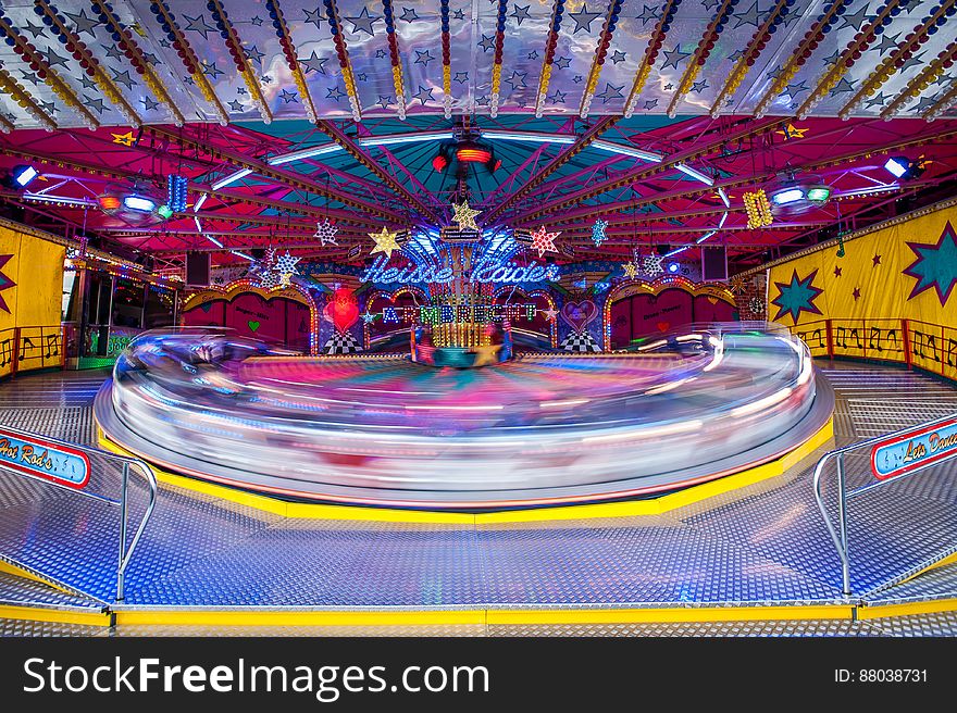 Roundabout marked above it by "Heisse Raider" in rapid motion creating blur, at a colorful funfair. Roundabout marked above it by "Heisse Raider" in rapid motion creating blur, at a colorful funfair.