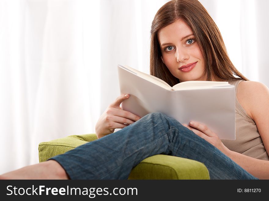 Young brunette reading book and sitting on green armchair. Young brunette reading book and sitting on green armchair