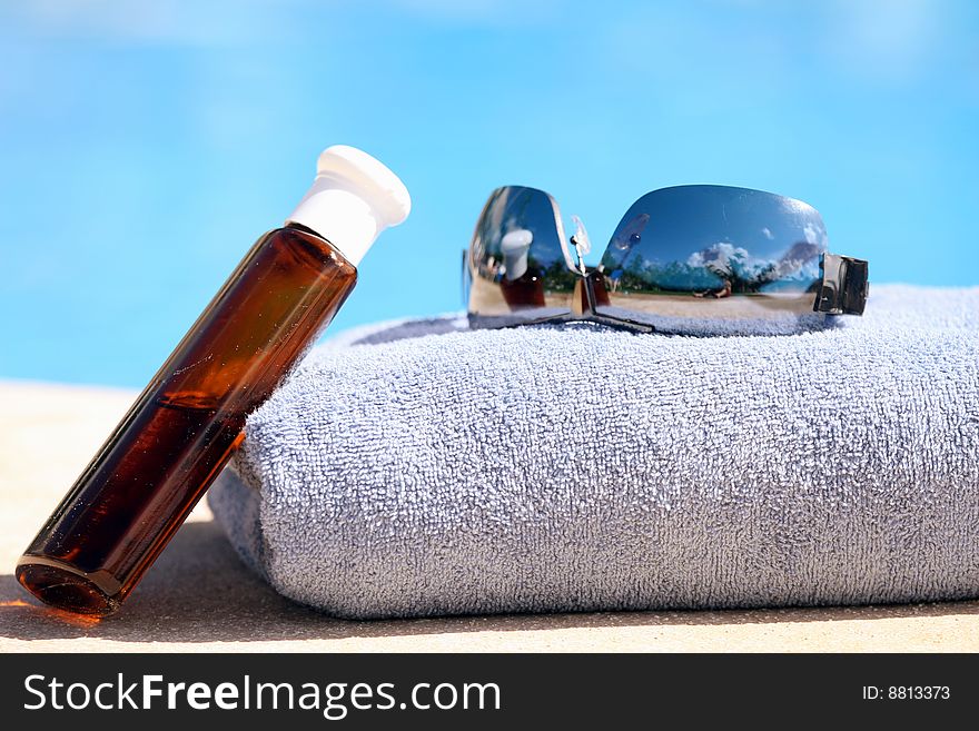 Sunglasses, towel and oil bottle by the swimming pool