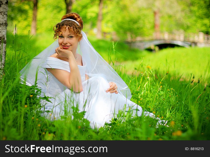Lucky bride sits on the grass in the park. Lucky bride sits on the grass in the park