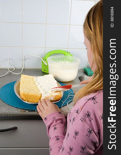 Girl is decorating a cake with whipped cream in the kitchen