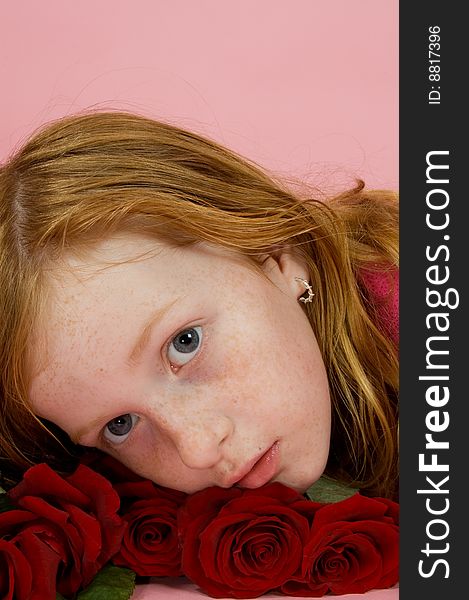 Red head girl laying on some red roses on pink background