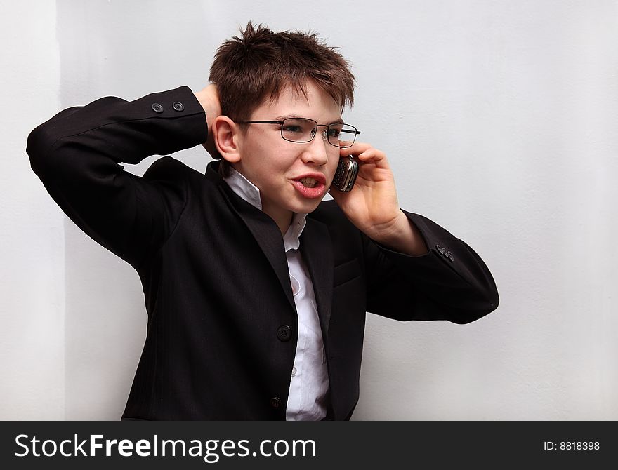 The boy in a business suit, points keeping a hand for a head and speaking by a mobile phone on a white background. The boy in a business suit, points keeping a hand for a head and speaking by a mobile phone on a white background