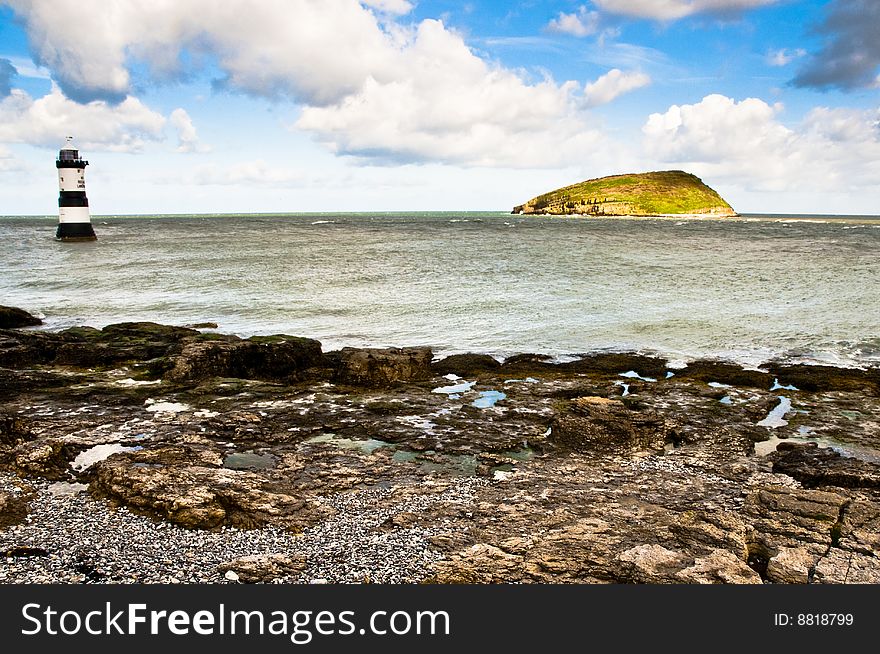 Puffin Island from the Isle of Anglesey with wave coming in over rocks with Penmon Lighthouse to the left