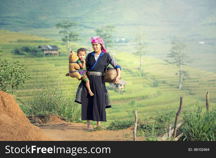An Asian farmer woman carrying a child near rice terraces. An Asian farmer woman carrying a child near rice terraces.