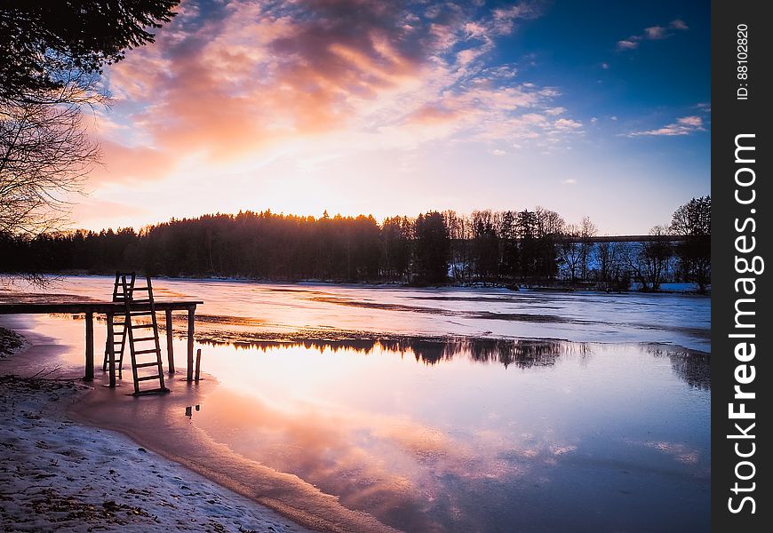 Wooden dock on river waterfront at dusk in countryside.