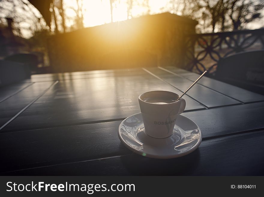 Coffee cup and saucer with spoon on tabletop outside at sunrise. Coffee cup and saucer with spoon on tabletop outside at sunrise.