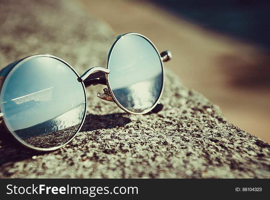 Closeup of round lenses in sunglasses on rock in sunshine.