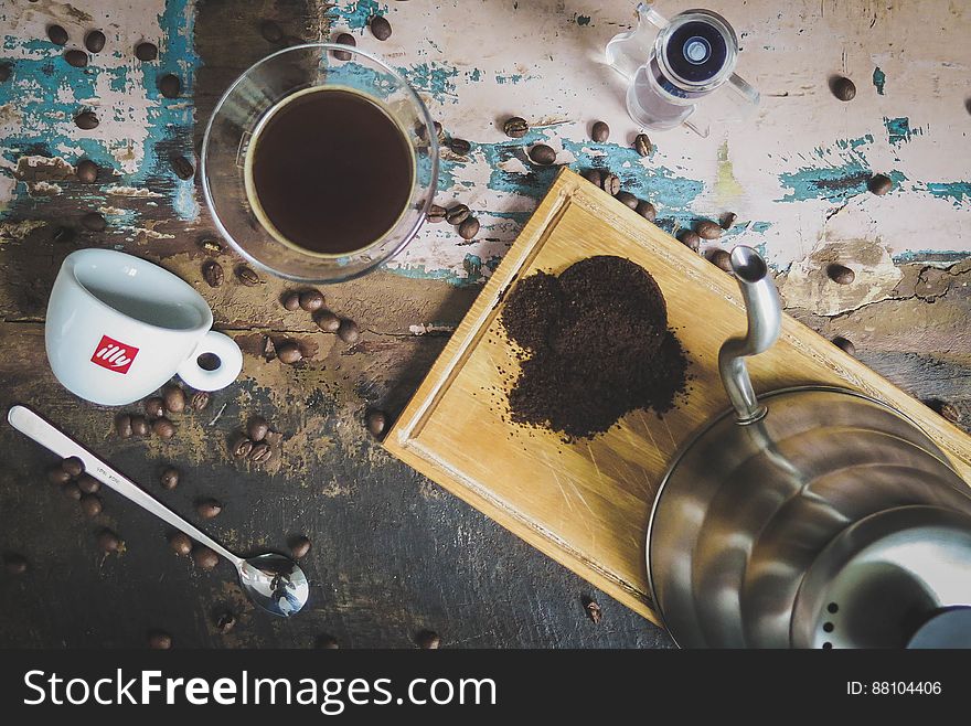 Coffee grinder, glass, grinded coffee, cup, teaspoon and coffee beans on a table. Coffee grinder, glass, grinded coffee, cup, teaspoon and coffee beans on a table.