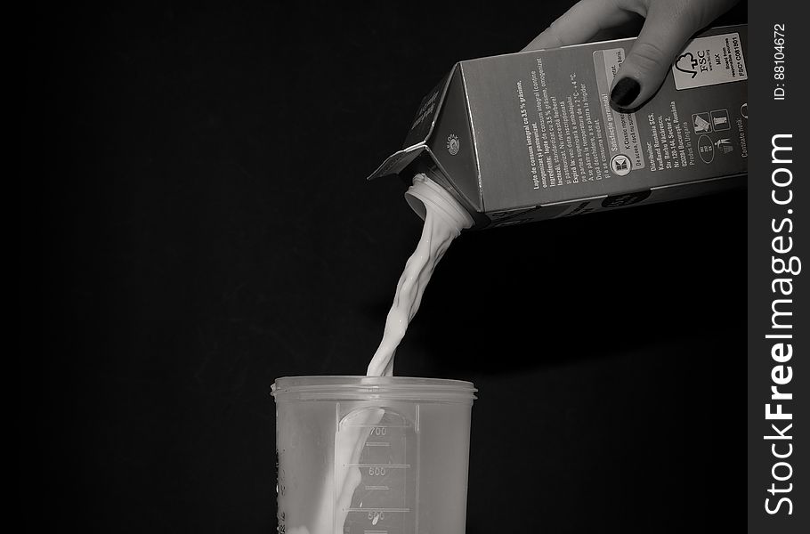A black and white close up of a woman`s hand pouring milk into a plastic cup. A black and white close up of a woman`s hand pouring milk into a plastic cup.
